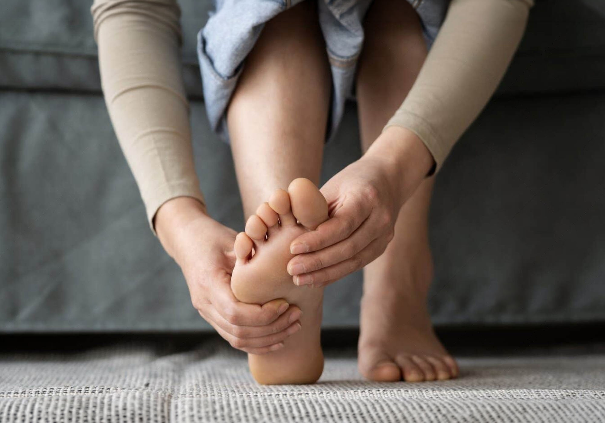 Person sitting on a couch massaging their foot.