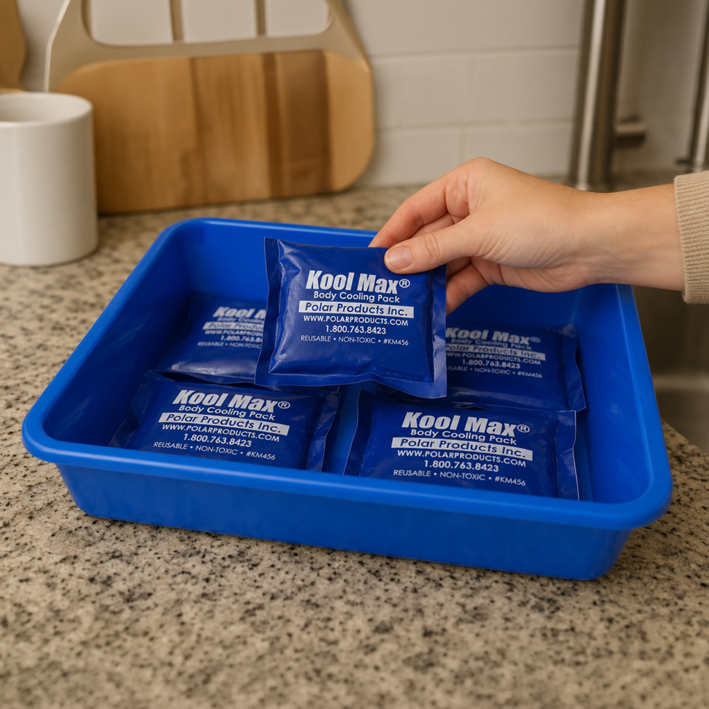 Person holding a Kool Max® cooling pack over a blue tray on a kitchen counter.