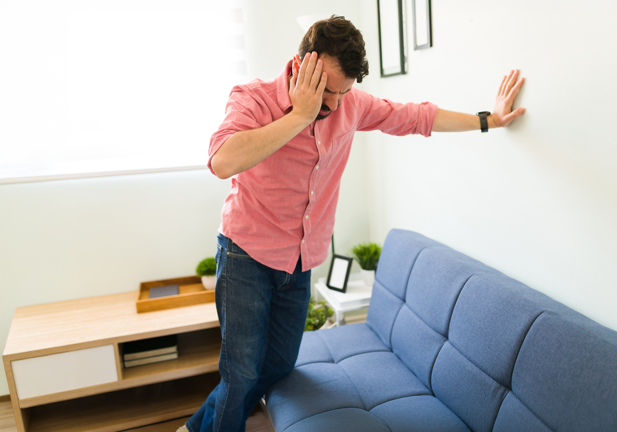 Man in a pink shirt and blue jeans standing in a living room with a blue couch.