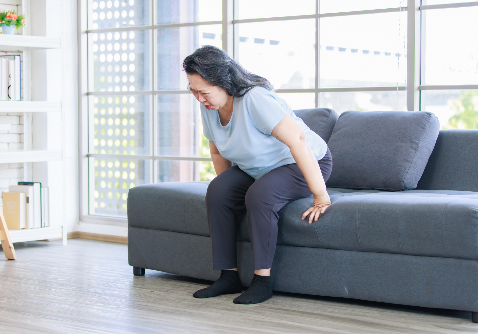 Woman stretching on a gray sofa in a bright living room.