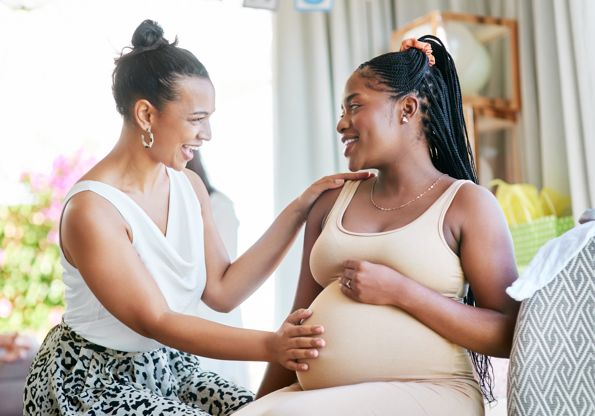 Two women interacting, one with her hand on the other's pregnant belly.