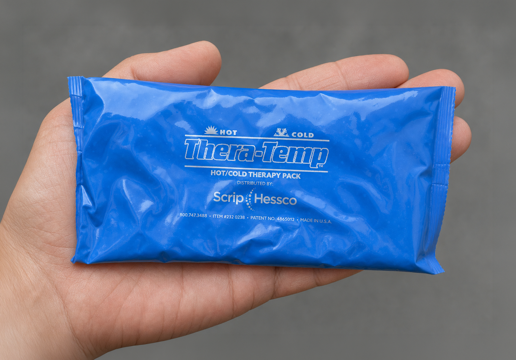A hand holding a blue Soft Ice® pack branded as Thera-Temp hot/cold therapy pack against a neutral gray background.