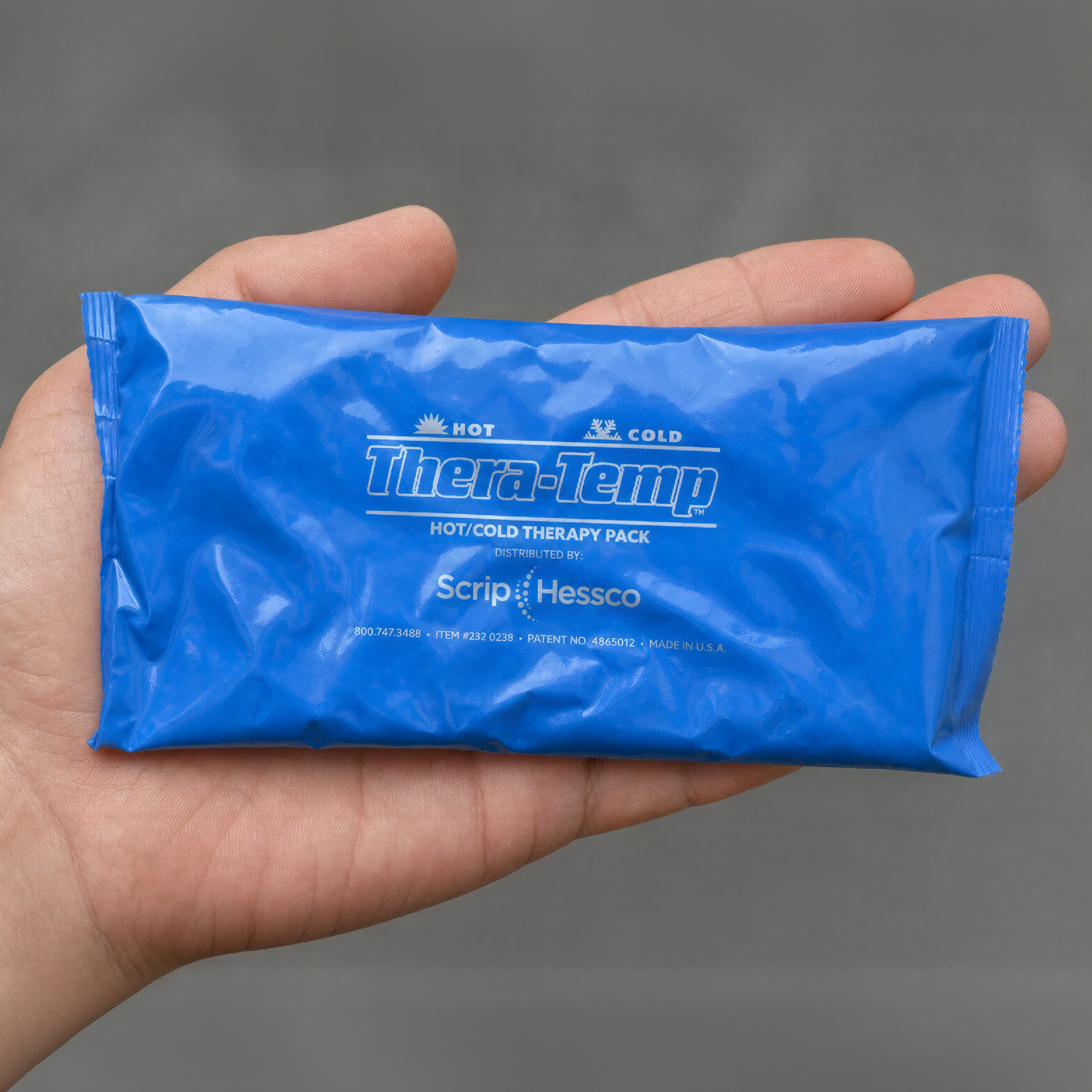 A hand holding a blue Thera-Temp hot/cold therapy pack against a neutral gray background.