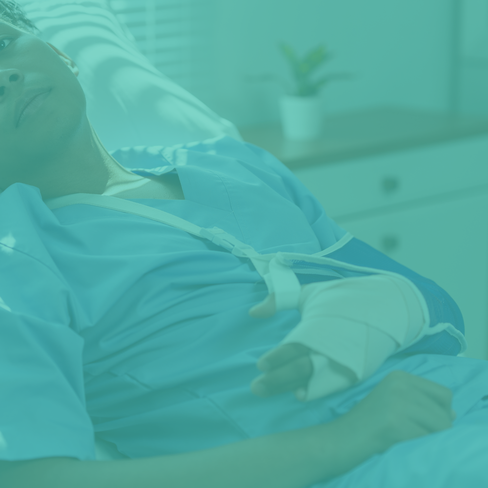 Person lying in bed with a bandaged arm, wearing a hospital gown with a teal overlay
