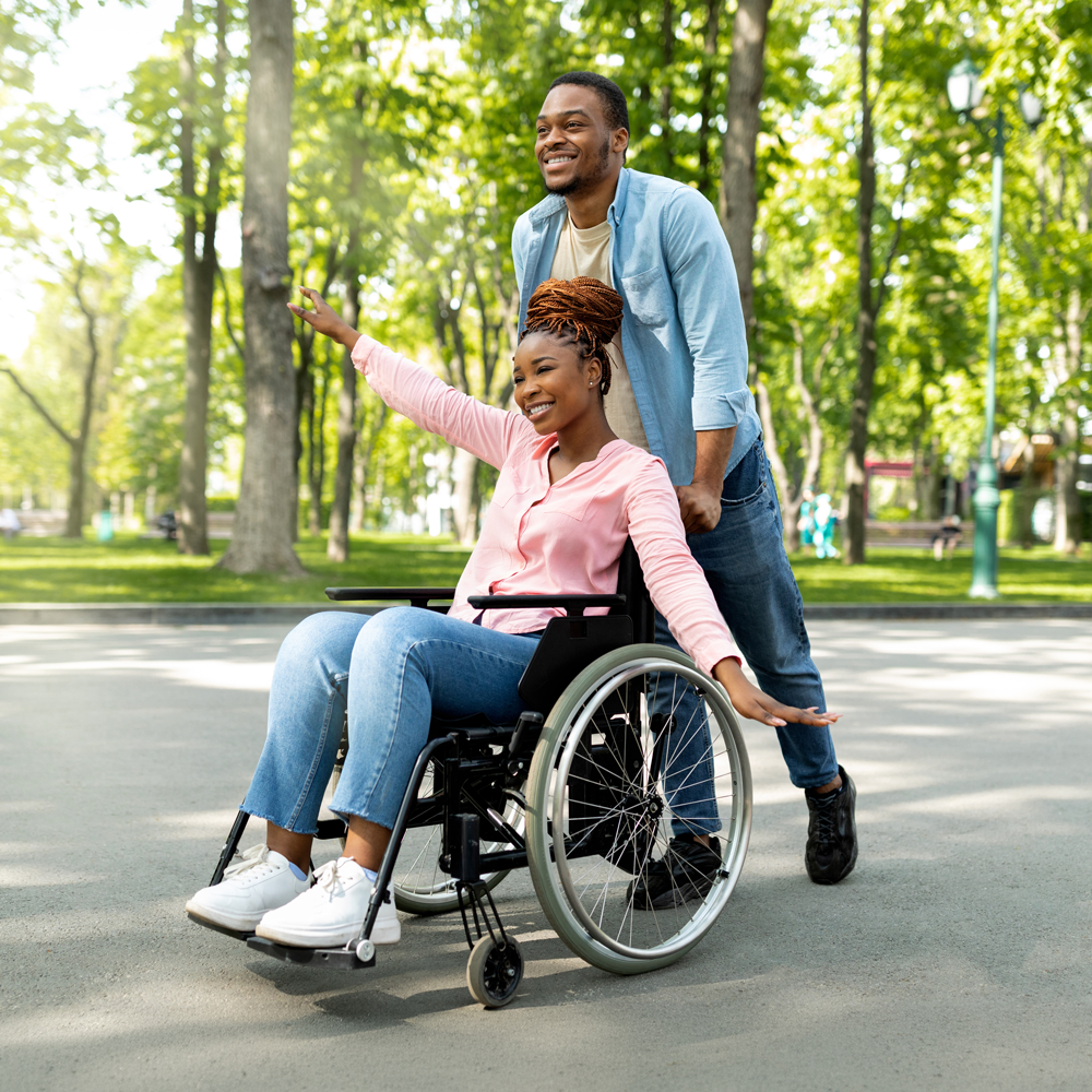 Person in a wheelchair being pushed by another person in a park