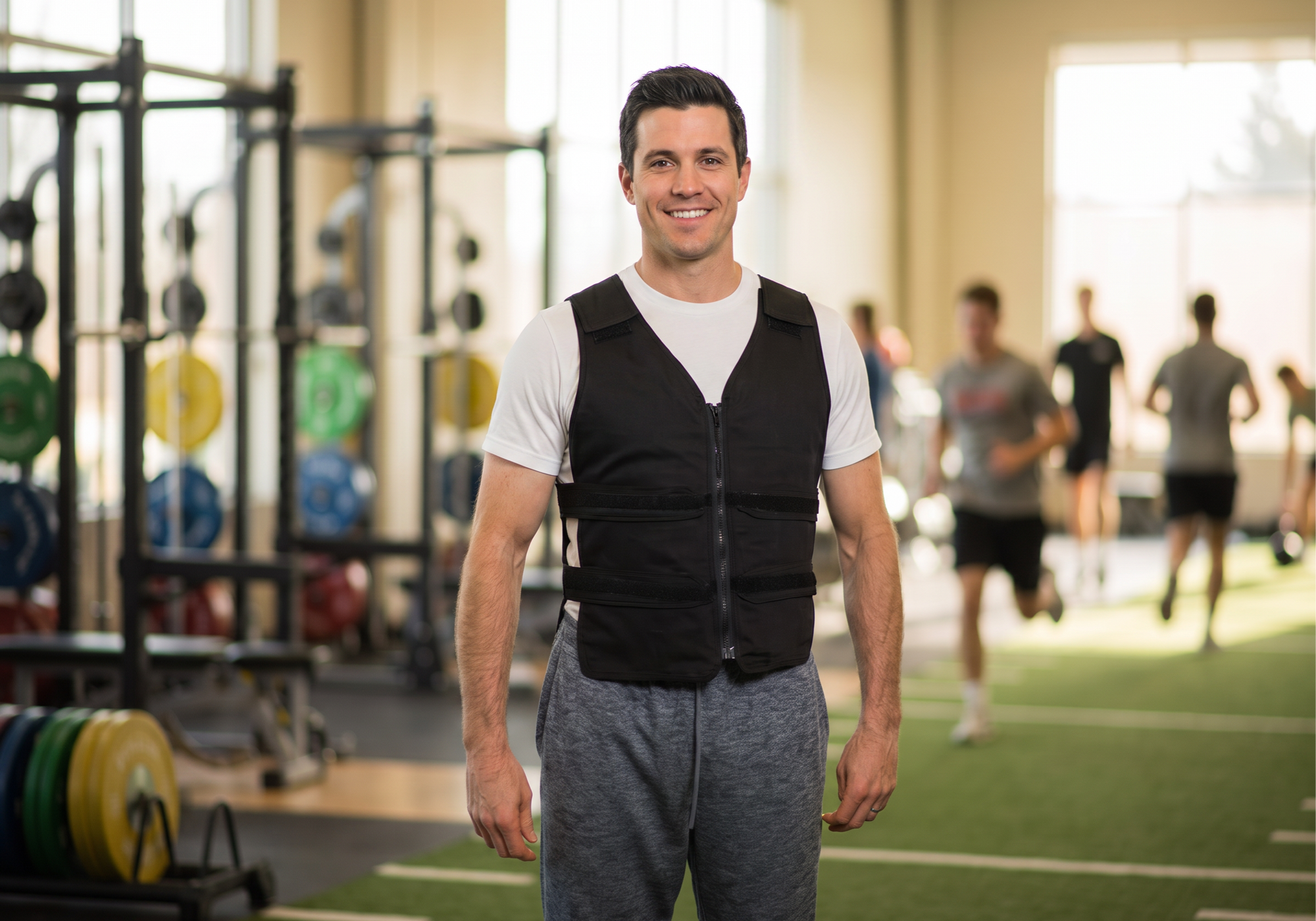 Man wearing a cooling vest in a gym setting with other people exercising in the background