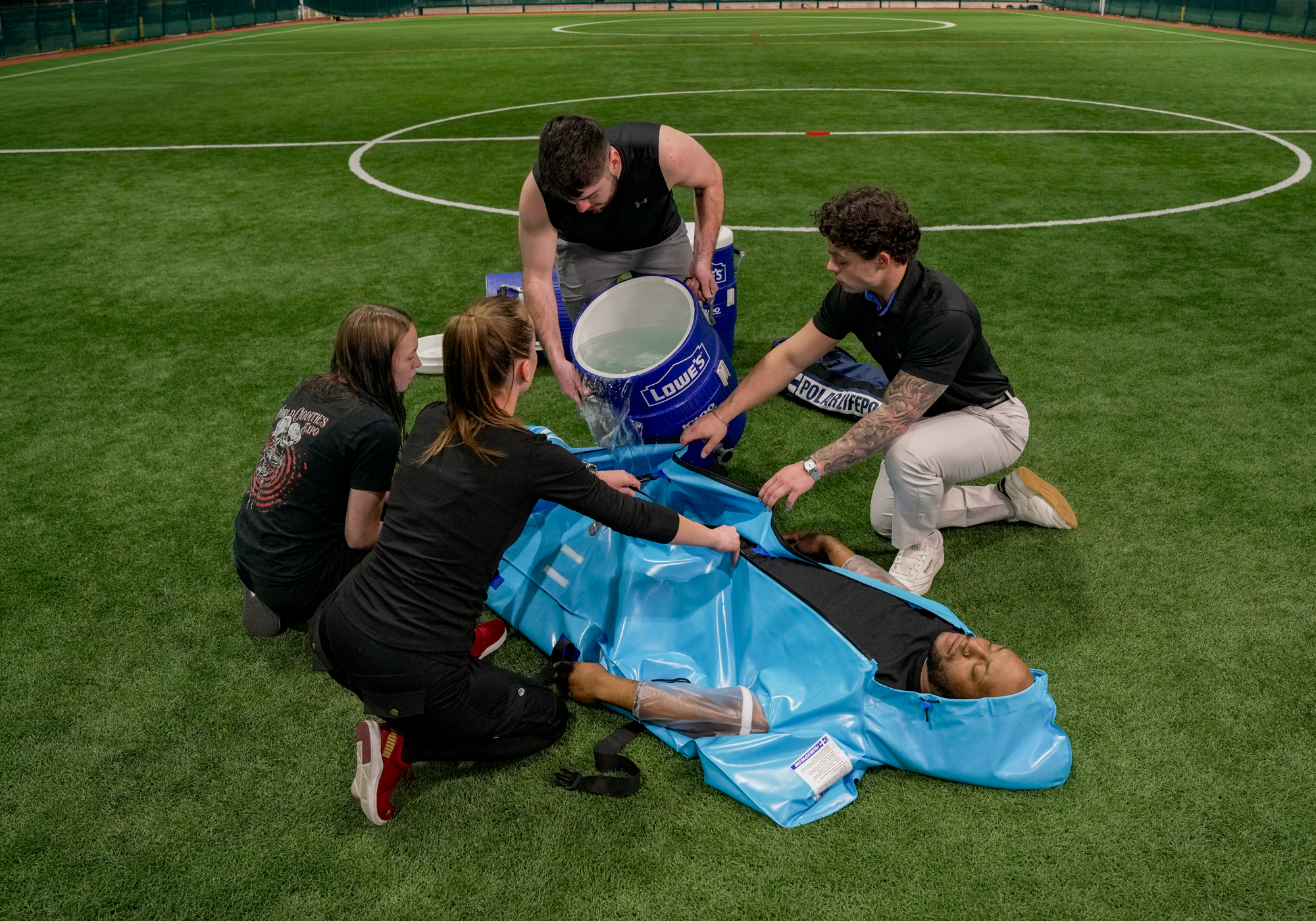 Group of people administering cold water immersion on a soccer field.