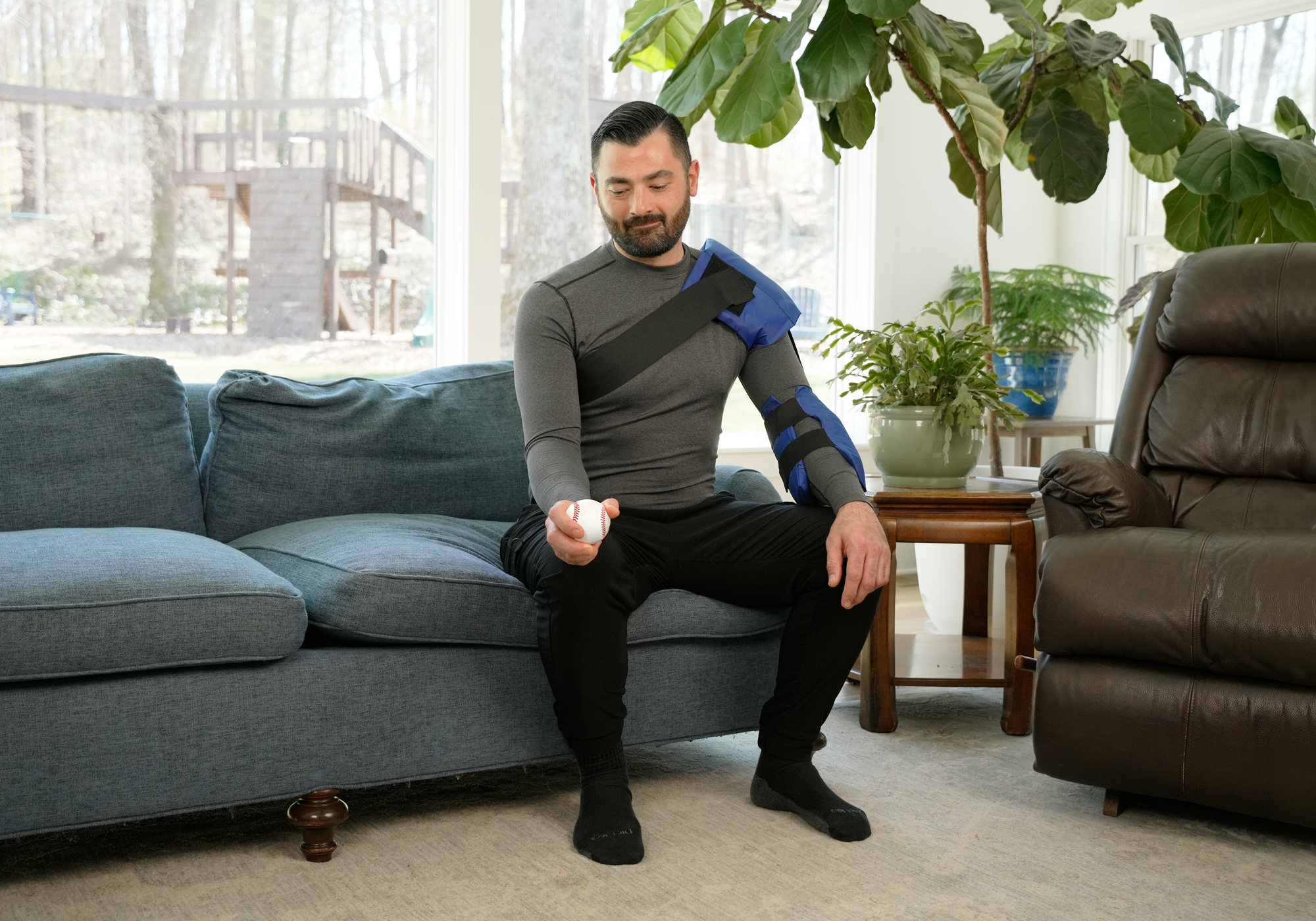 Man sitting on a couch with a cold therapy pack over his shoulder in a living room.