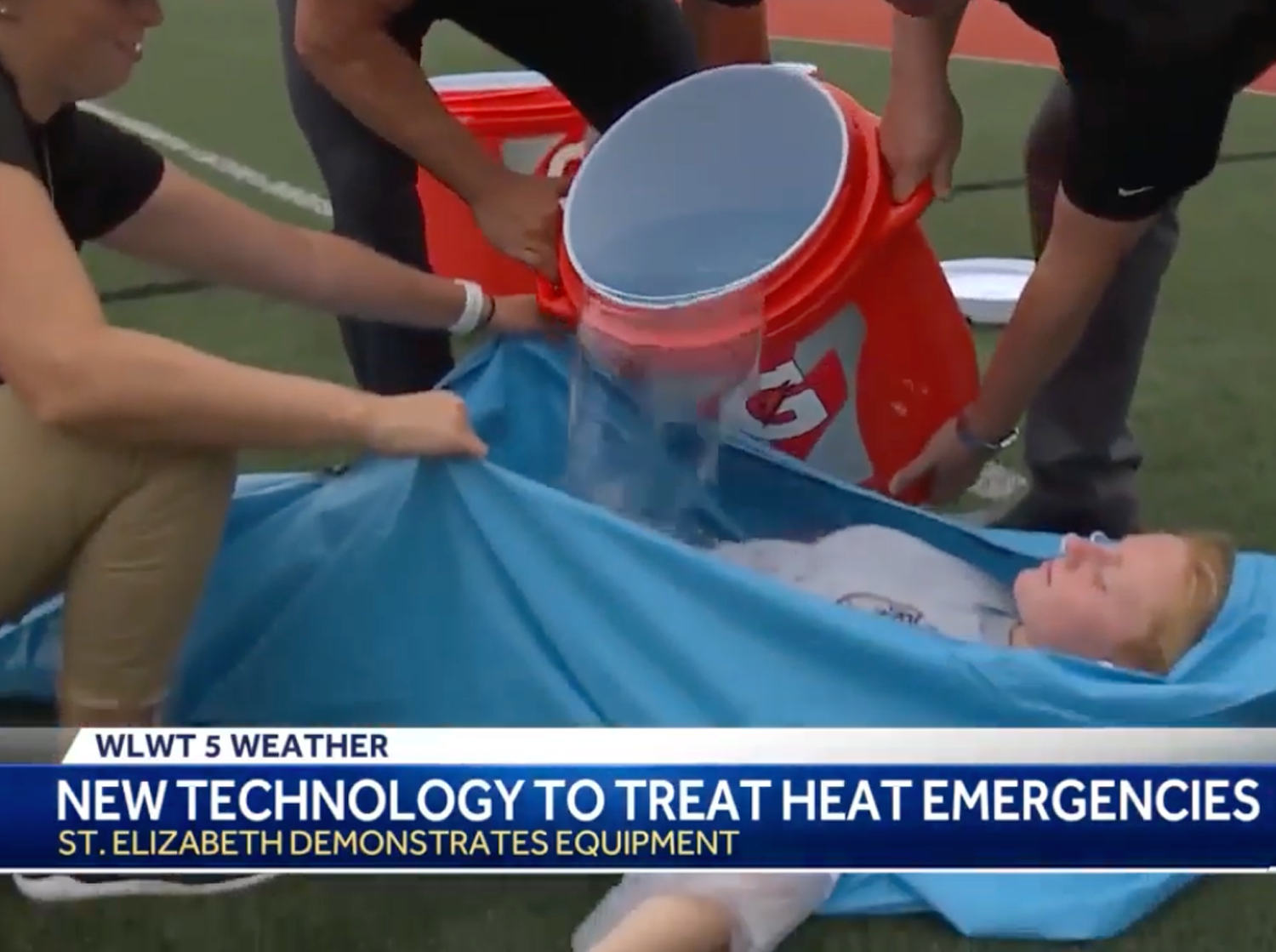 A person lying in a blue Polar Life Pod® on a sports field while others pour water from an orange cooler. A news banner at the bottom reads 'WLWT 5 WEATHER NEW TECHNOLOGY TO TREAT HEAT EMERGENCIES'.
