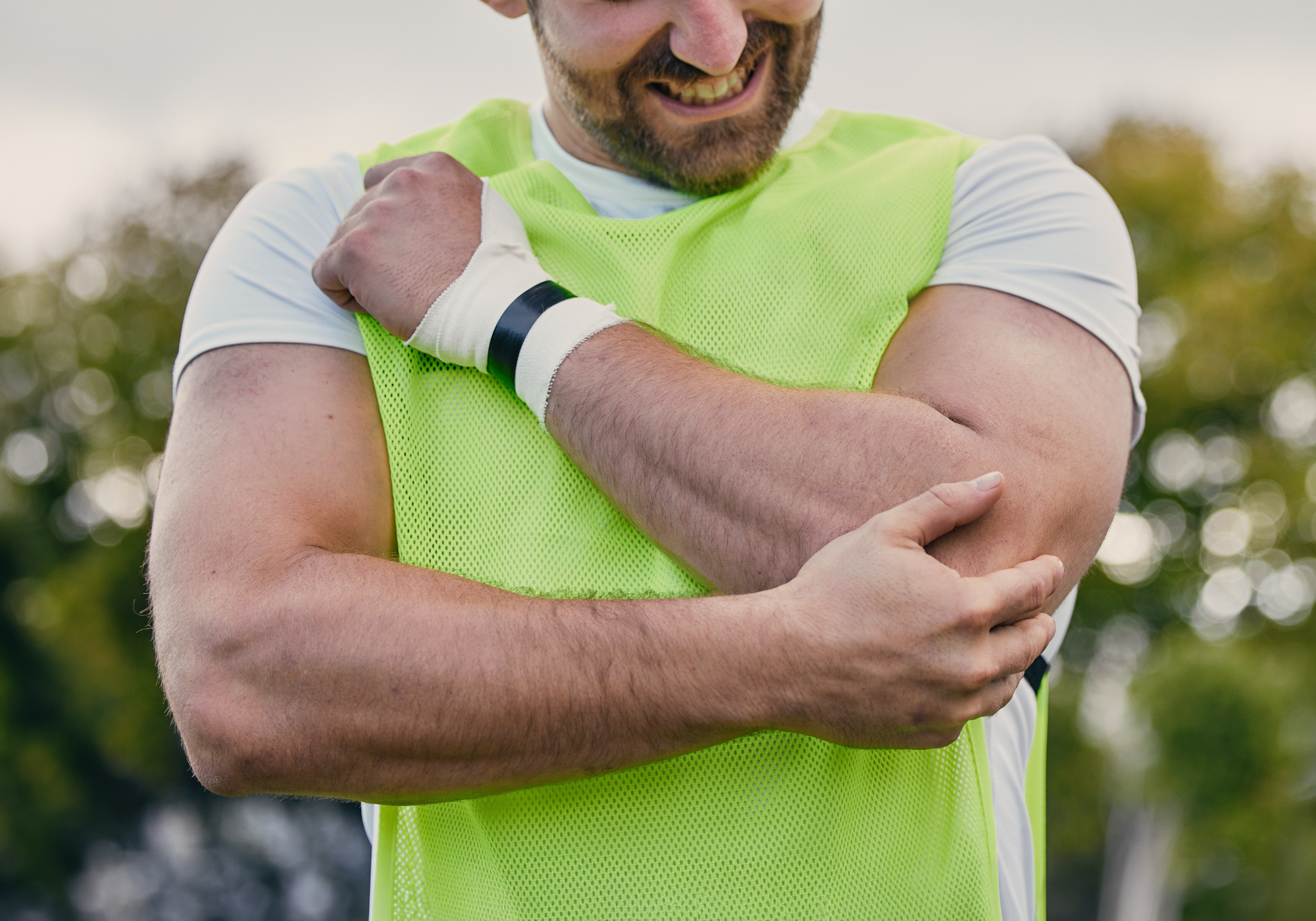 Man in a bright green vest holding his arm, with a blurred outdoor background