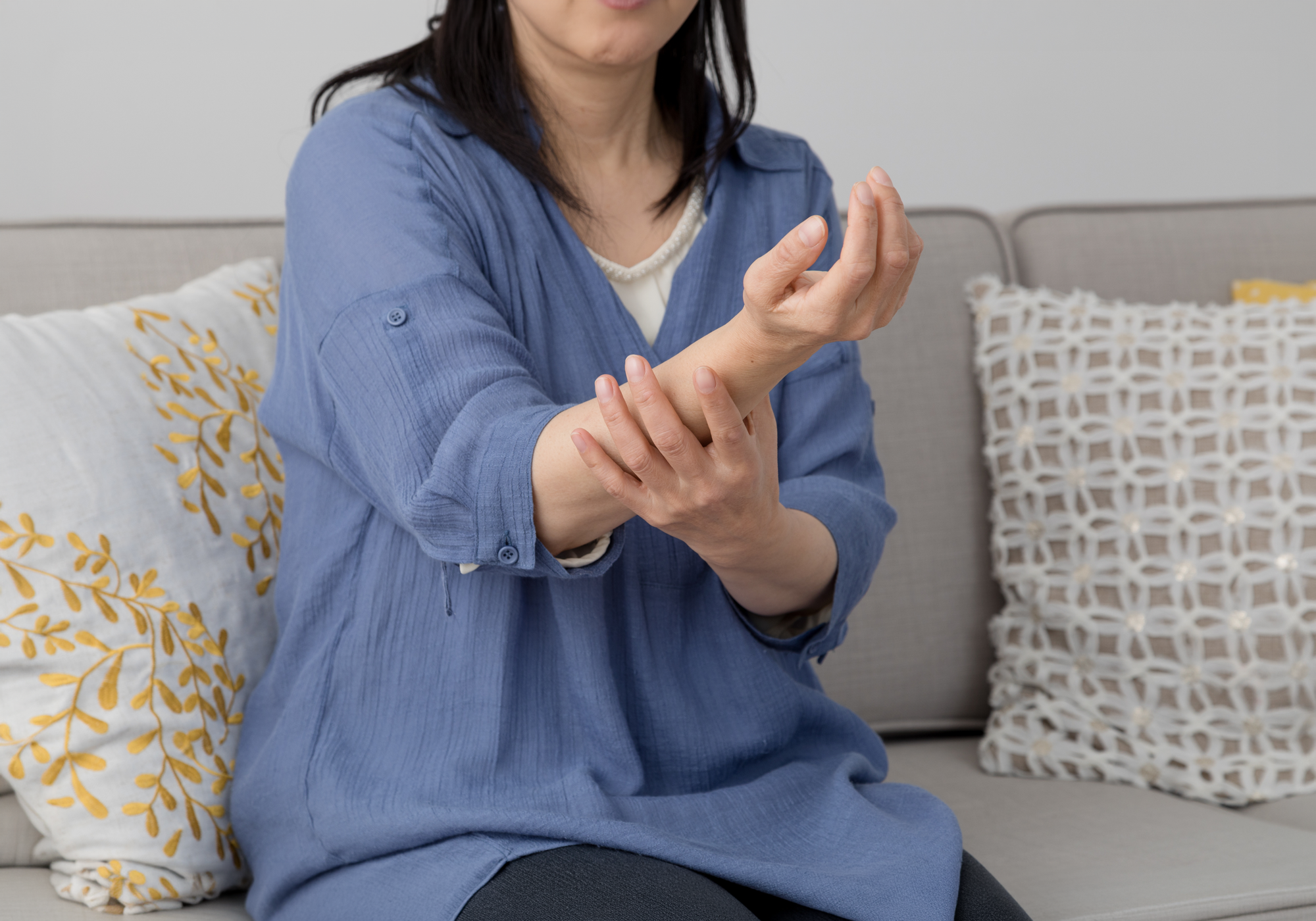 Woman sitting on a couch holding her wrist, possibly experiencing pain or discomfort.