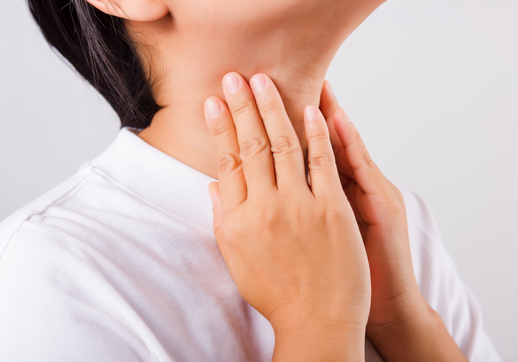 Person touching their neck with both hands on a light background