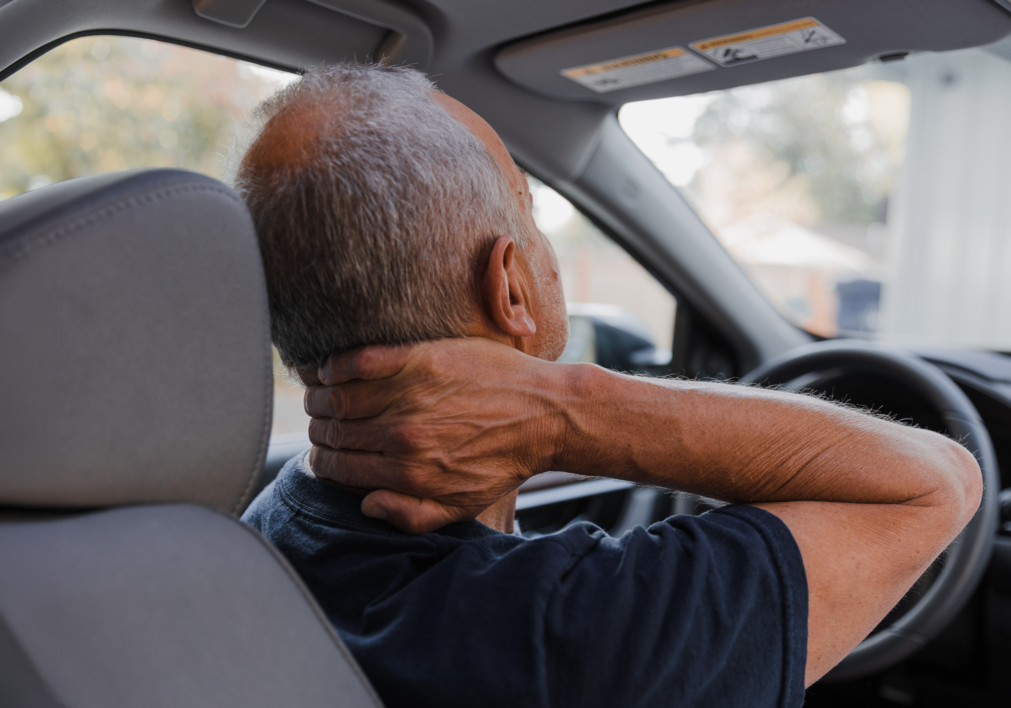 Man sitting in a car with his head and neck in discomfort