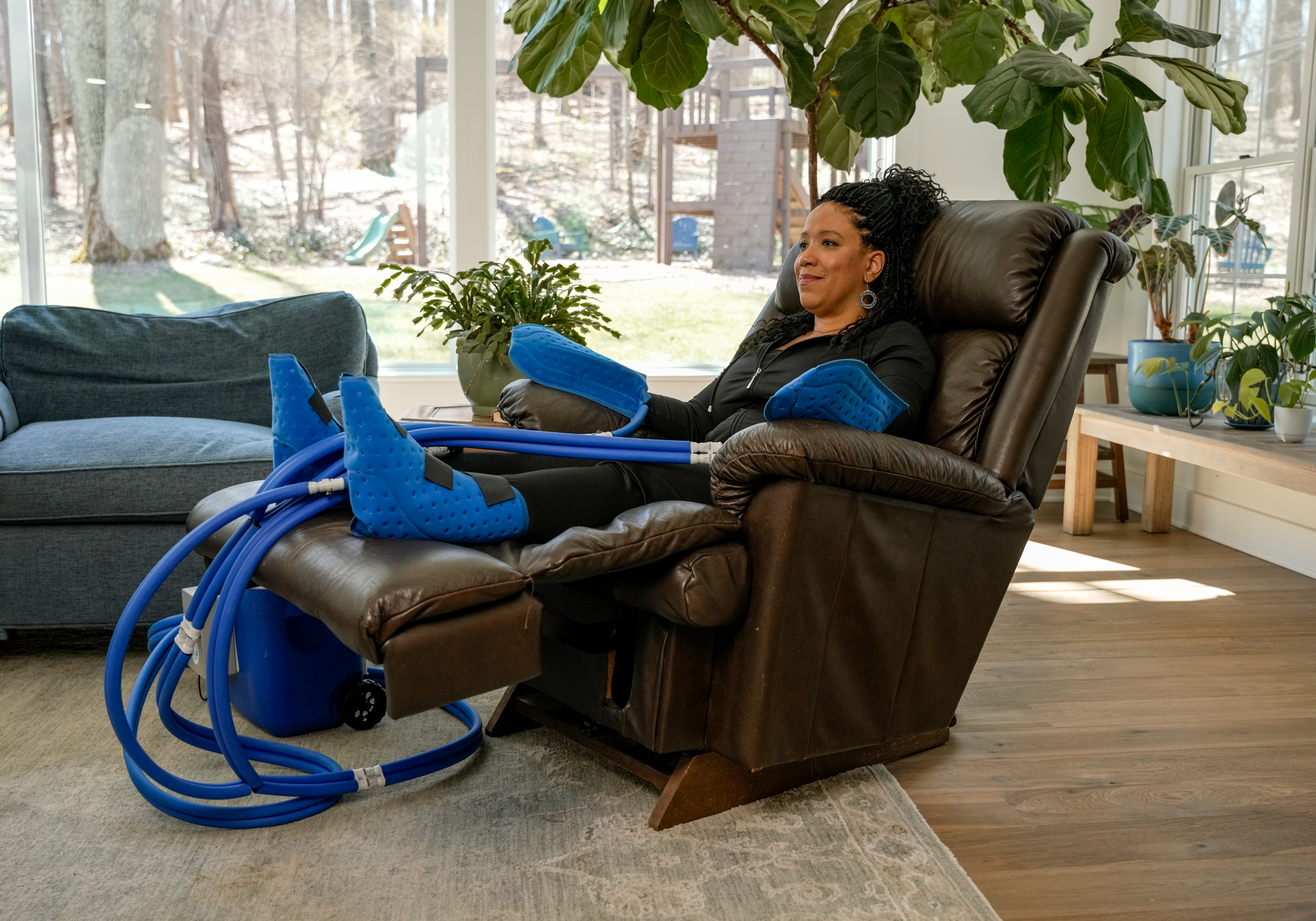 Person sitting in a recliner with an Active Ice extremities cooling system, surrounded by plants in a bright room.